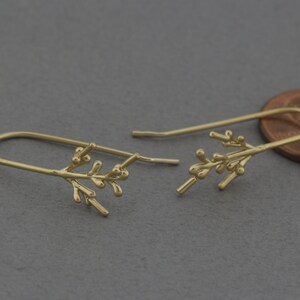 May include: A pair of gold-toned earrings with a delicate branch design. The earrings are made of a thin wire with small, round beads representing leaves.