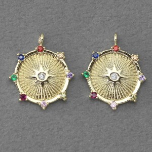 Puede incluir: Dos colgantes de tono dorado con un diseño de estrella y un centro de cristal transparente. Cada colgante está rodeado de ocho piedras preciosas de colores.