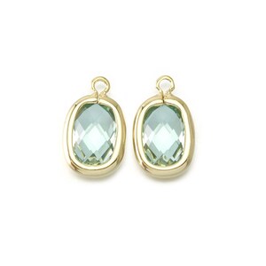 Può includere: Due ciondoli ovali color oro, ognuno con un cristallo sfaccettato verde chiaro.