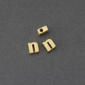 May include: Three gold-colored metal letter beads, two are the letter 'n' and one is a spacer bead.