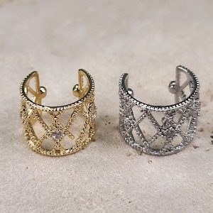 May include: Two ear cuffs, one gold and one silver, with a geometric design and small clear stones.