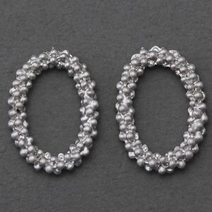 May include: A pair of silver oval-shaped earrings made of small beads.