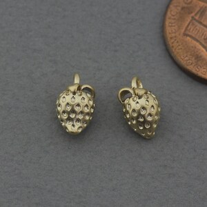 Puede incluir: Dos abalorios de fresa de color dorado con superficie texturizada. Los abalorios son pequeños y tienen un bucle en la parte superior para sujetarlos a un collar o pulsera.