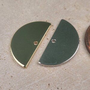 May include: Two half-circle metal charms, one gold and one silver, with a hole in the center. The charms are about the size of a US penny.