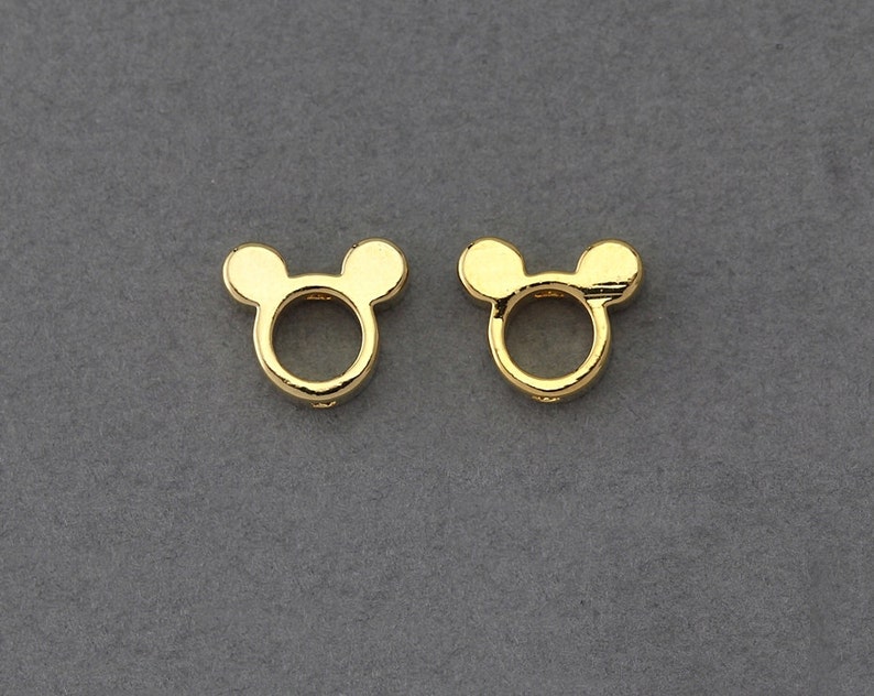 May include: Two gold-coloured metal charms shaped like Mickey Mouse heads with a circular opening in the centre.