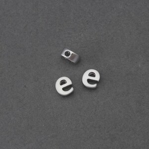 May include: Three silver letter beads spelling the letter "e". The beads have a hole in the top for stringing.