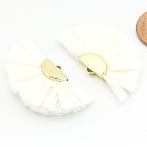May include: Two white fabric fan-shaped embellishments with gold metal half-circle clasps.
