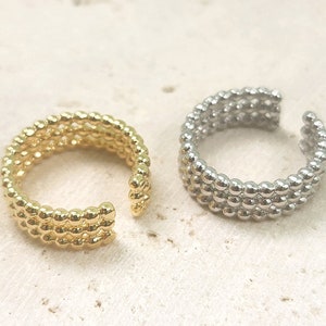 Könnte beinhalten: Zwei verstellbare Ringe aus kleinen Perlen. Ein Ring ist golden und der andere ist silber.