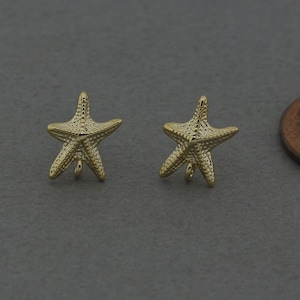 May include: A pair of gold-tone starfish earrings with a textured surface. The earrings are about the size of a US penny.
