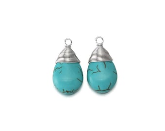 Op de afbeelding: Twee turquoise blauwe traanvormige oorbellen met zilverdraad gewikkeld rond de bovenkant van elke oorbel.