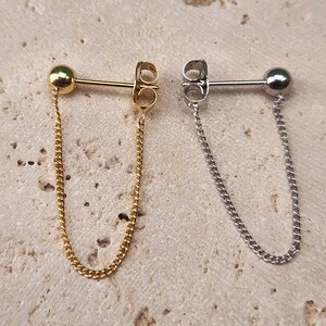 Puede incluir: Dos pares de pendientes colgantes con una pequeña bola en la parte superior y una cadena que cuelga. Un par es dorado y el otro es plateado.
