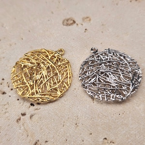 Puede incluir: Dos colgantes redondos de metal con un diseño delicado e intrincado de alambre. Un colgante es dorado y el otro es plateado.