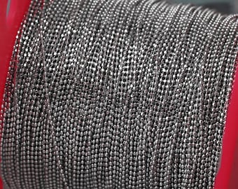 May include: A close-up of a silver chain, wound around a red spool. The chain is made of small, round links.