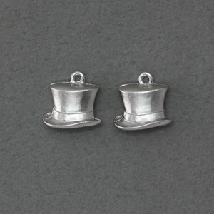 May include: Two silver top hat charms. The charms are detailed with a band around the hat and a loop at the top for attaching to a necklace or bracelet.