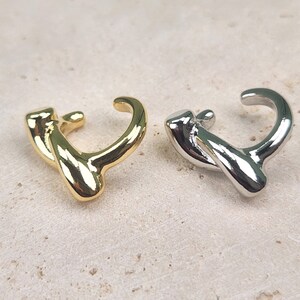 May include: Two ear cuffs, one gold and one silver, in a twisted, abstract design.