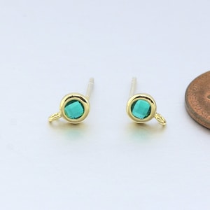 May include: A pair of gold-toned earrings with a small green gemstone in the center of each earring. The earrings have a small loop on the side for attaching to a hook.