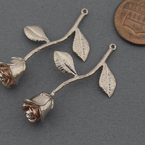 May include: Two silver rose charms with a loop at the top for attaching to jewelry. The roses have a textured finish and are a light gold color.