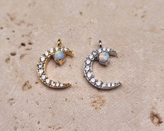 May include: Two crescent moon charms with a small opal stone in the center. One charm is gold with clear stones around the crescent moon and the other charm is silver with clear stones around the crescent moon.