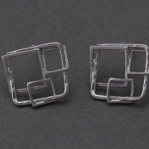 May include: A pair of silver earrings with a geometric design featuring multiple overlapping squares.