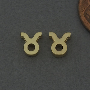 Puede incluir: Un par de pendientes de color dorado con el signo del zodíaco Tauro. Los pendientes son pequeños y delicados, y son perfectos para añadir un toque de estilo a cualquier atuendo.