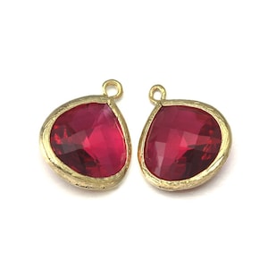May include: Two gold-toned pendant charms with a teardrop shape and a red crystal in the centre.