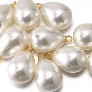 May include: A group of ten white pearlescent teardrop-shaped beads with gold-colored metal loops at the top.