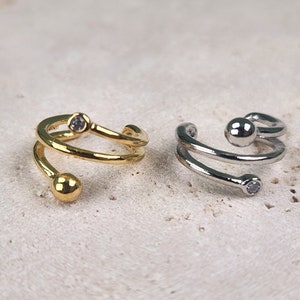 May include: Two ear cuffs, one gold and one silver, with a spiral design and a small clear rhinestone on each cuff.