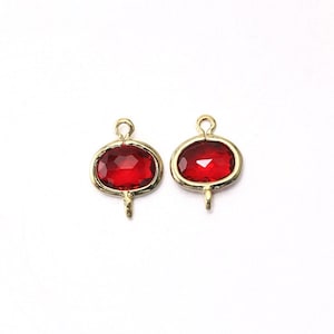 Pode incluir: Dois pingentes ovais dourados com pedras de vidro vermelho. Cada pingente tem um laço na parte superior e um pequeno laço na parte inferior.