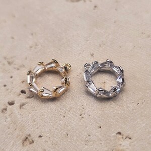Pode incluir: Dois pingentes de prata e ouro com um design circular e detalhes de cristal transparente.