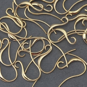 May include: A collection of gold-coloured earring hooks, each featuring a distinctive, curved design. The hooks are scattered in a random arrangement, creating an aesthetically pleasing composition.