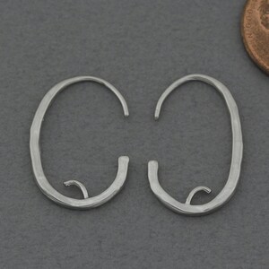 May include: A pair of silver hoop earrings with a hammered finish. The hoops are oval shaped and have a slightly irregular shape.