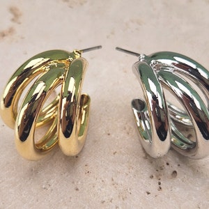 Puede incluir: Un par de pendientes de aro con un diseño de aro triple. Un pendiente es dorado y el otro es plateado.