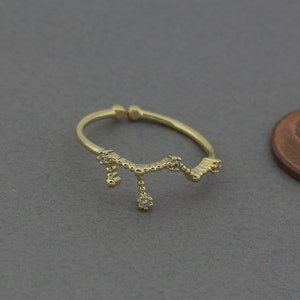 May include: A gold ring with a delicate design featuring a series of small, connected circles and a dangling charm with a small clear stone.