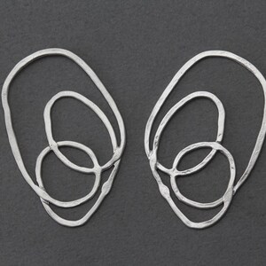 May include: A pair of silver earrings with a unique, abstract design featuring three interlocking circles.