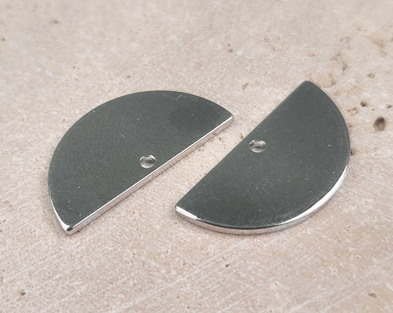 May include: Two silver metal half-circle shapes with a hole in the center. The shapes are smooth and shiny.