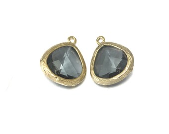 May include: Two gold-toned pendant charms with a dark gray faceted glass stone in the center. The stone is set in a textured gold-toned frame.