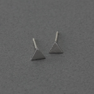 May include: A pair of silver triangle stud earrings. The earrings are small and simple, with a brushed finish.