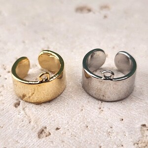 May include: Two metal rings with a jump ring attached. The ring on the left is gold and the ring on the right is silver.