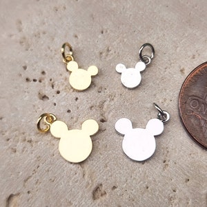 May include: Four small metal charms in the shape of Mickey Mouse heads. Two charms are gold and two are silver.