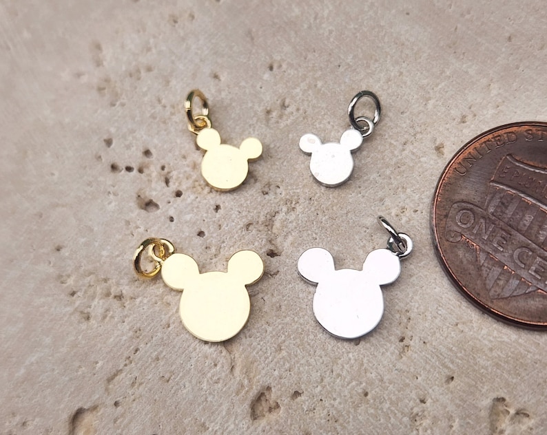May include: Four small metal charms in the shape of Mickey Mouse heads. Two charms are gold and two are silver.