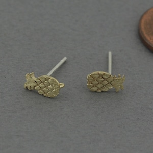 May include: A pair of gold pineapple stud earrings. The earrings are small and delicate, and they would make a great gift for a friend or loved one.
