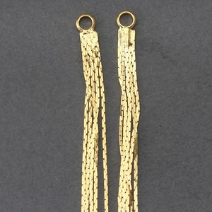 May include: Two gold chain necklaces with a delicate, multi-strand design. Each necklace has a small, round clasp.