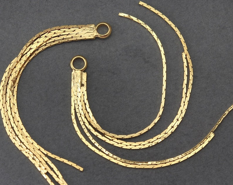 May include: Two gold chain tassel earrings with multiple strands of chain. The chains are connected at the top with a small gold loop.