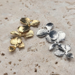 Peut inclure: Deux ensembles de breloques en forme de fleur d'orchidée, l'un en or et l'autre en argent. Les breloques sont détaillées et réalistes, avec des pétales délicats et une finition texturée.