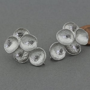 Puede incluir: Un par de pendientes de plata con un grupo de cinco elementos texturizados, redondeados y en forma de cuenco.