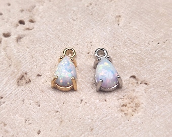 May include: Two teardrop-shaped opal charms, one with a gold setting and one with a silver setting. The opals are iridescent and have a white base.