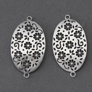 May include: Two silver oval-shaped metal charms with a delicate floral cutout design. The charms have two small loops at the top and bottom.