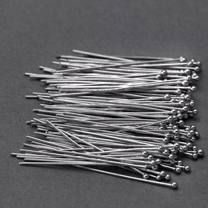 May include: A pile of silver-colored head pins with round heads. The pins are arranged in a random pattern and are all the same size.