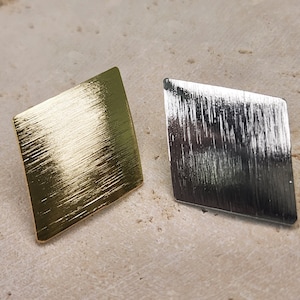 May include: Two diamond-shaped earrings, one gold and one silver, with a brushed finish.