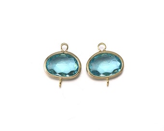 Op de afbeelding: Twee ovale, lichtblauwe glazen bedels met gouden metalen frames en springringen. De bedels zijn perfect om een ​​toets van kleur en glans toe te voegen aan sieradenprojecten.